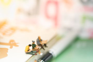 Miniature people: Small businessmen reading book and sitting on notebook. Education, Money, Financial and Business Growth concept.
