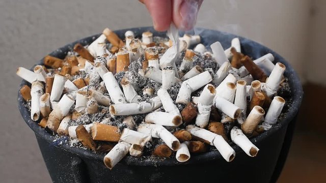 Slow-motion footage of an ashtray full of cigarettes and a hand erasing a cigarette, with some smoke.