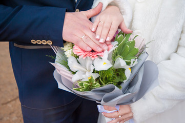 hands of the bride and groom on a bouquet of flowers