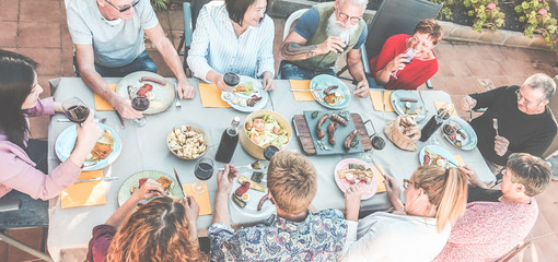 Top view of happy family eating and drinking wine at barbecue dinner outdoor - Multiracial people...