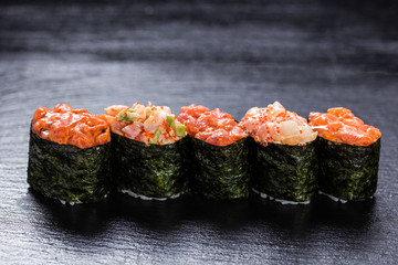 Shrimp, salmon, scallop, tuna gunkanmaki stacked side by side against slate backround