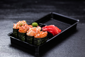 Shrimp, salmon, scallop, tuna gunkanmaki in take-away container against slate backround