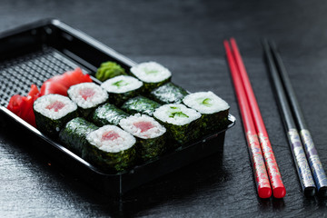 Maki placed in a delivery container next to two pair of chopsticks