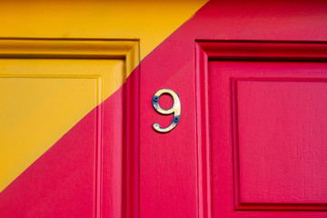 House number nine on a brightly painted red and yellow wooden house door with a diagonal stripe and...