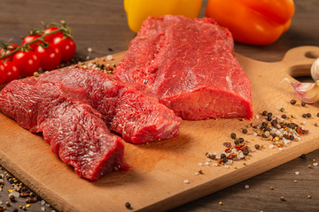 Raw beef on a wooden background with spices and vegetables.