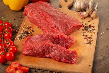 Raw beef on a wooden background with spices and vegetables.