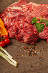 Raw beef on a wooden background with spices and vegetables.