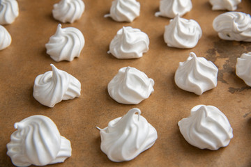 Small, round, raw meringues in rows on brown baking paper 
