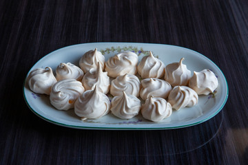 Rustic plate with twirl meringue cookies on the dark brown table contrasting