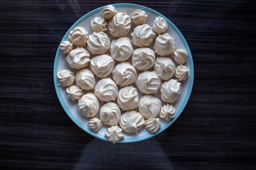 Top down view of round plate of meringue cookies on dark background