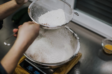 Bakery concept. Working woman weighing and sifting the ingredients of her sponge cake. Lifestyle.