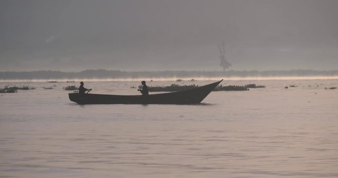The silhouettes of African fishermen in the early morning sun in a traditional wooden canoe on Lake Victoria with mist on the water.