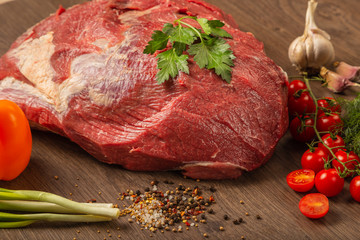 Raw beef on a wooden background with spices and vegetables.
