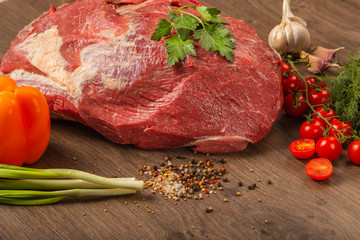 Raw beef on a wooden background with spices and vegetables.