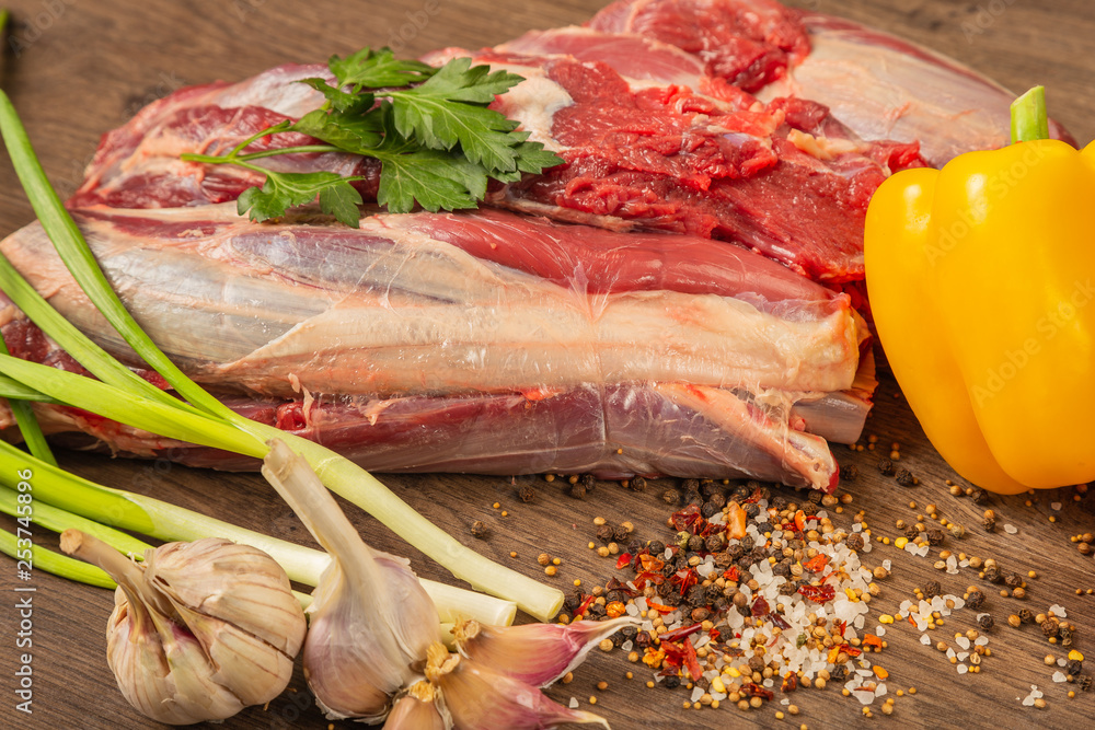 Wall mural raw beef on a wooden background with spices and vegetables.