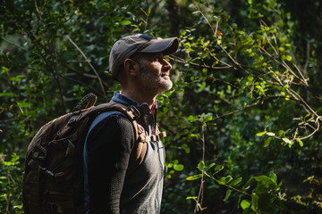 Man with backpack hiking in a beautiful forest with sunlight, side view