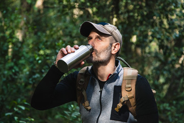 Hiker in a green wild forest taking water from a bottle