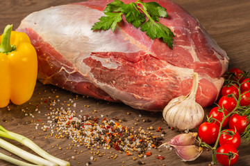 Raw beef on a wooden background with spices and vegetables.