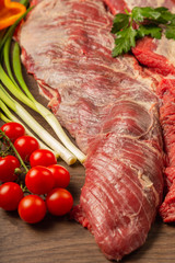 Raw beef on a wooden background with spices and vegetables.