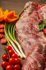 Raw beef on a wooden background with spices and vegetables.