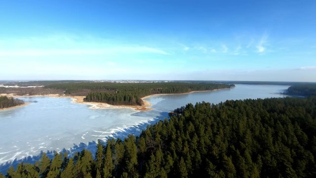 A beautiful aerial backward shot of a landscape with an enourmous frozen lake and spruce forest during winter, Poland.