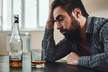 Obraz premium Whether you think you can or you think you can’t, you’re right. Drunk man with glass and bottle of whiskey sitting at table in kitchen. Drinking alone. Male alcoholism concept