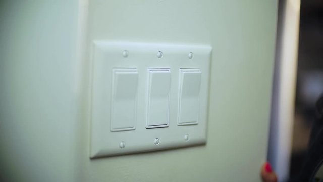 A close up of a female hand enters frame and wipes a light switch on a wall with a paper towel.