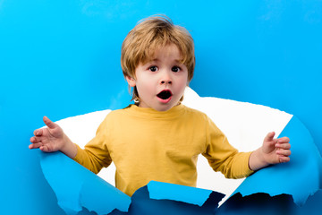 Surprised boy looking through hole in paper wall. Shocked child boy making hole in paper. Adorable kid looks through hole. Blonde small toddler looks through ripped paper. Sale, discount, season sales