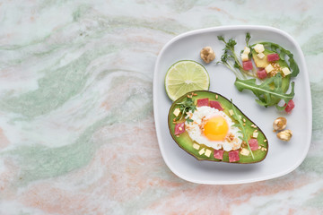 Baked Avocado boat with ham cubes, quail egg and cheese served with green rucola salad