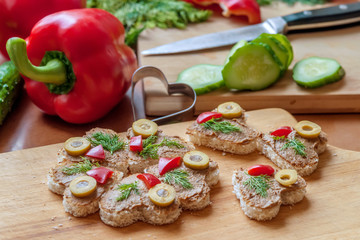 heart shaped canape with liver pate, decorated with olives, sweet peppers and dill, cooking at home, close up