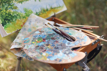 Palette and easel with brushes in nature