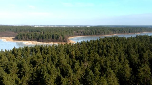 A zoomed in aerial view of an enourmous frozen lake and vast forest during winter season, Poland.