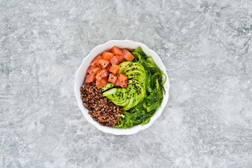 Poke bowl. Ingredients: salmon, avocado, brown rice, seaweed. Gray background, top view, space for text