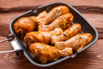 Raw chicken drumsticks in sauce and spices in a pan not a wooden background.