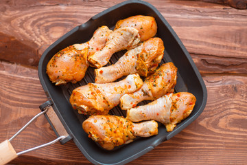Raw chicken drumsticks in sauce and spices in a pan not a wooden background.