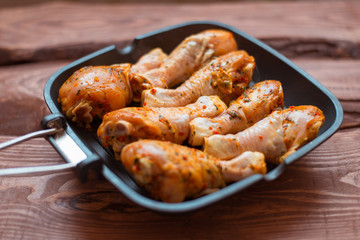 Raw chicken drumsticks in sauce and spices in a pan not a wooden background.