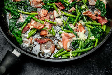 Peas sprouts, young spinach leaves fried in a pan together with a crispy, bacon-flavored
