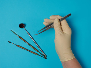 Dental instruments in tray and dentist hand on blue background