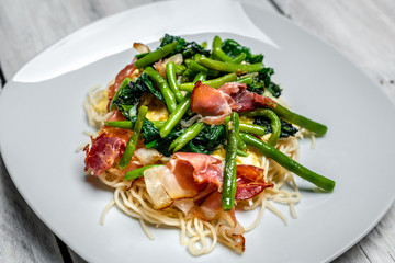 Spaghetti carbonara with pieces of crispy bacon, garlic, fresh spinach leaves and sprouts of green, young peas