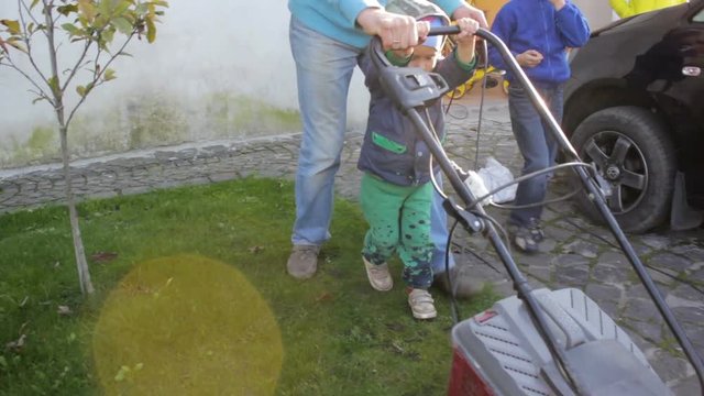 sons help to mow the grass, Little boy with his father mowing the lawn by a lawn mower in the yard