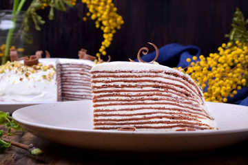 Piece of chocolate crepes cake with cream cheese on a white plate