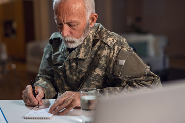 Senior army soldier taking notes at office desk.