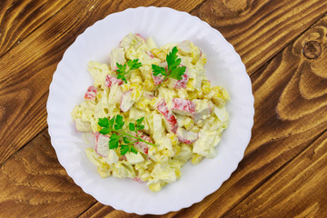 Salad with crab sticks, sweet corn, chinese cabbage, eggs and mayonnaise on wooden table