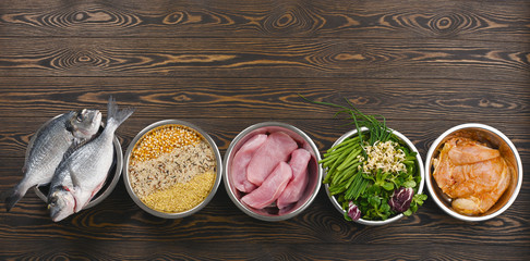 Panorama banner with healthy pet food ingredients with chopped raw turkey, fish, groats, greens and...