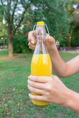 Cropped image of a girl who is holding and opening a bottle of fresh juice outside