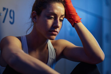 Pensive athletic woman resting in locker room after sports training.