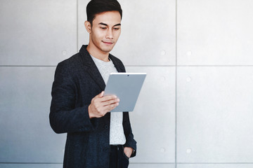 Portrait of Young Happy Businessman Using Digital Tablet. Standing by the Industrial Concrete Wall. Reading Data and Smiling