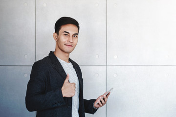 Young Happy Businessman Smiling and Show Thumbs Up while Using Smartphone. Standing by the...