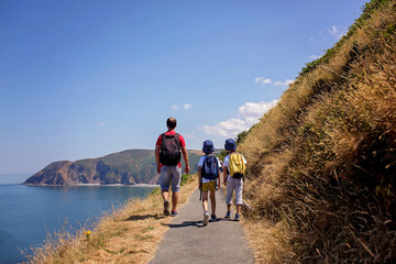Father and two boys, family walking on a small path along the stunning Devonshire coastline near...
