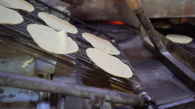 Freshly stamped corn tortillas falling from the cutter and going onto the griddle part of the machine.